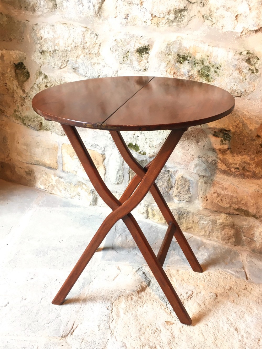 A Victorian mahogany folding occasional table with a hinged circular top supported by curved X-frame legs.