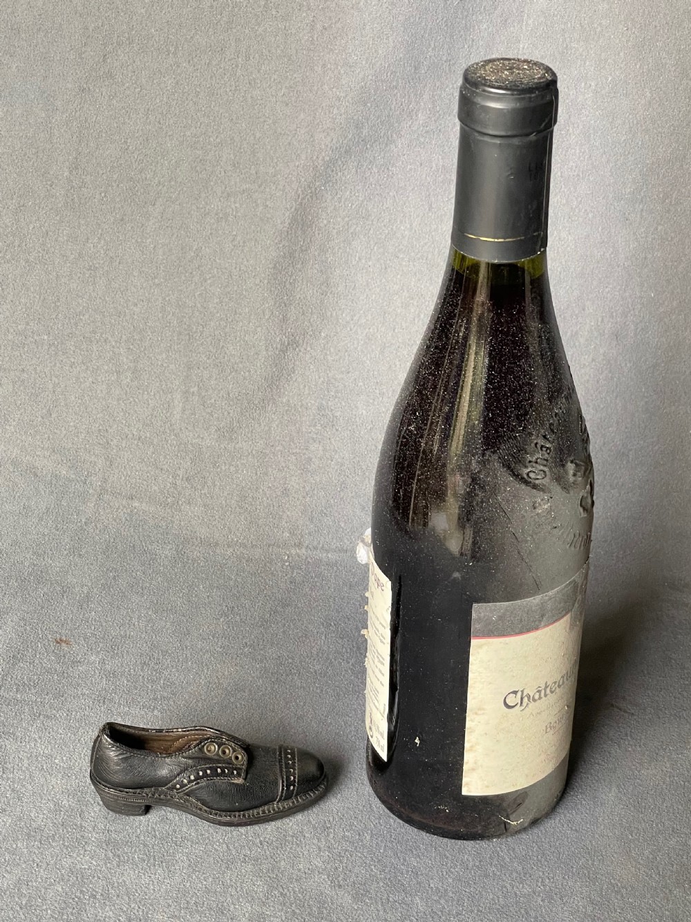 A miniature black leather shoe crafted with brogue stitching and metal eyelets displayed next to a coin for scale. View II