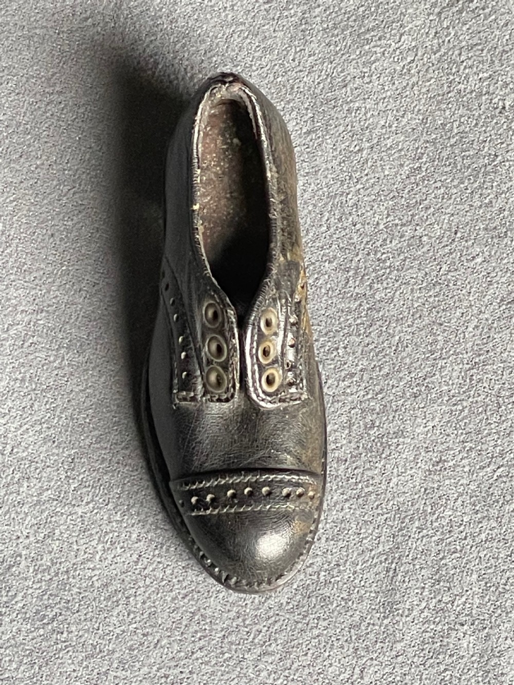 A miniature black leather shoe crafted with brogue stitching and metal eyelets displayed next to a coin for scale. View III