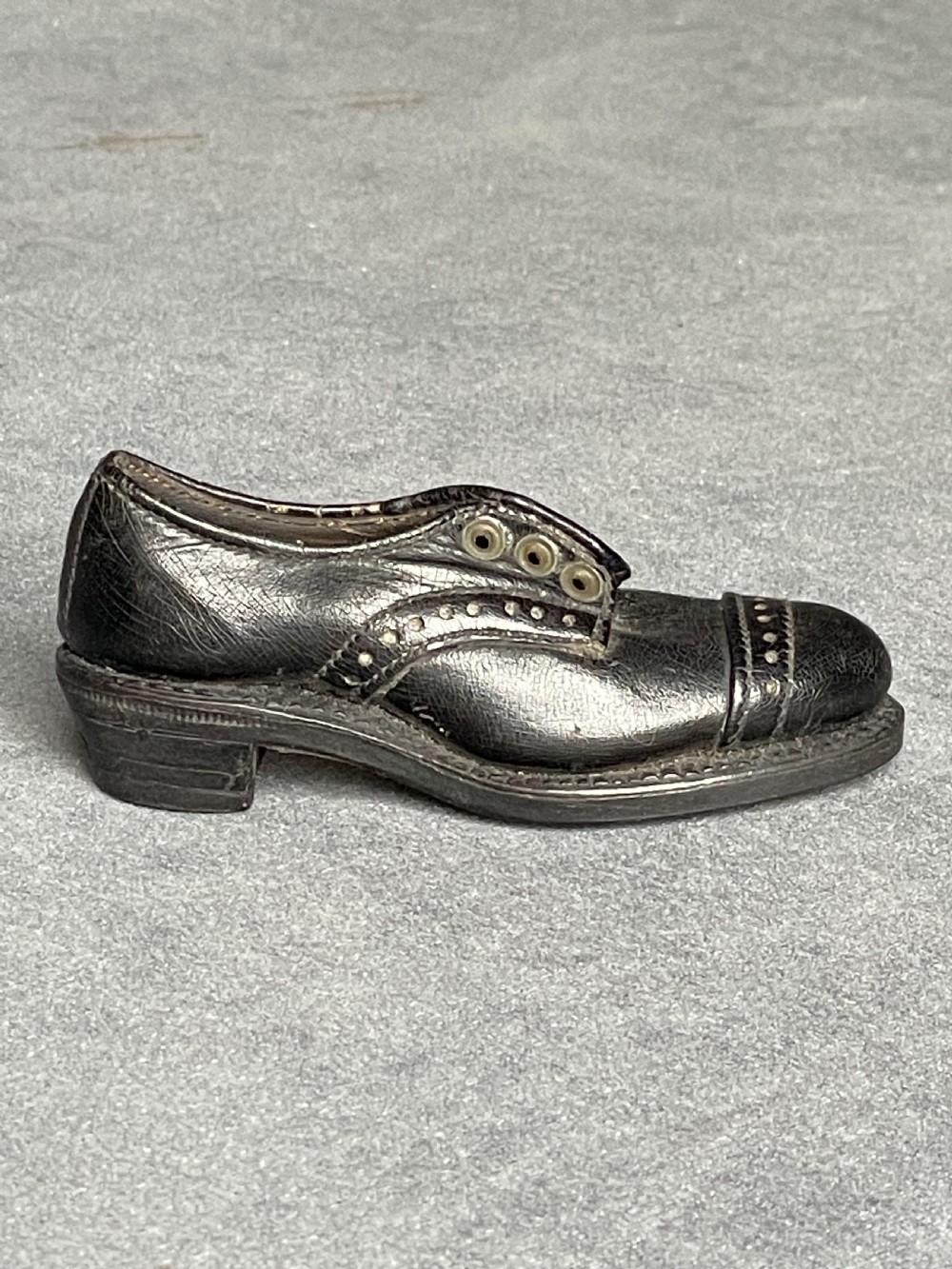 A miniature black leather shoe crafted with brogue stitching and metal eyelets displayed next to a coin for scale. View V