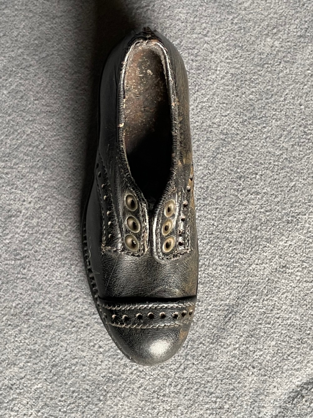 A miniature black leather shoe crafted with brogue stitching and metal eyelets displayed next to a coin for scale. View IX