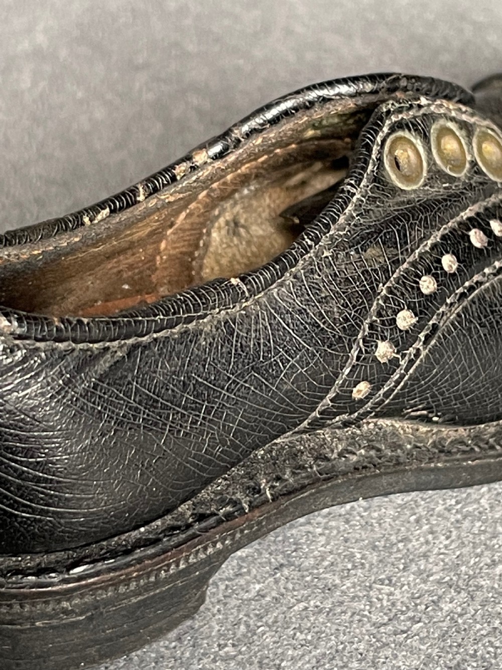 A miniature black leather shoe crafted with brogue stitching and metal eyelets displayed next to a coin for scale. View XI