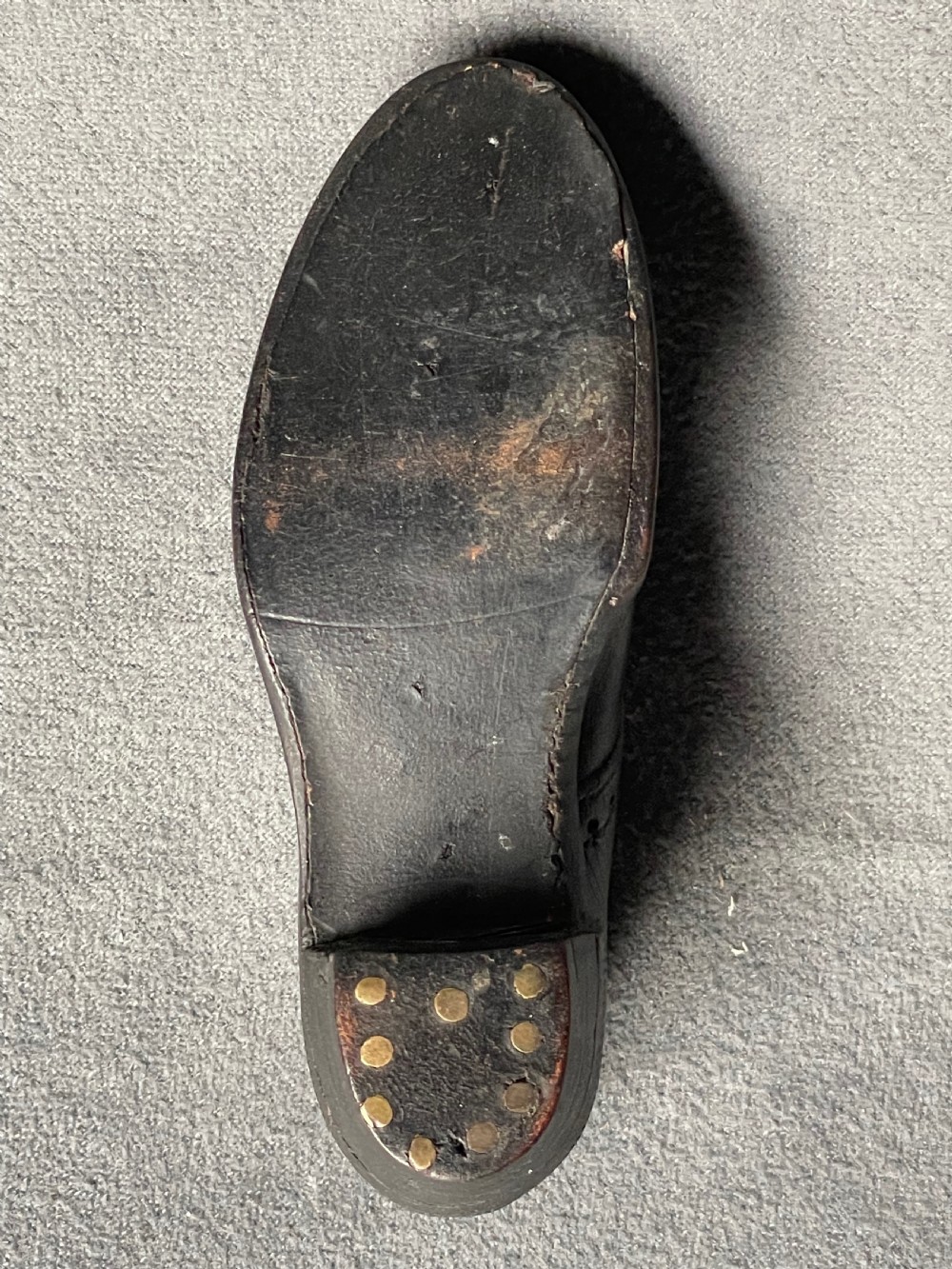 A miniature black leather shoe crafted with brogue stitching and metal eyelets displayed next to a coin for scale. View XIII