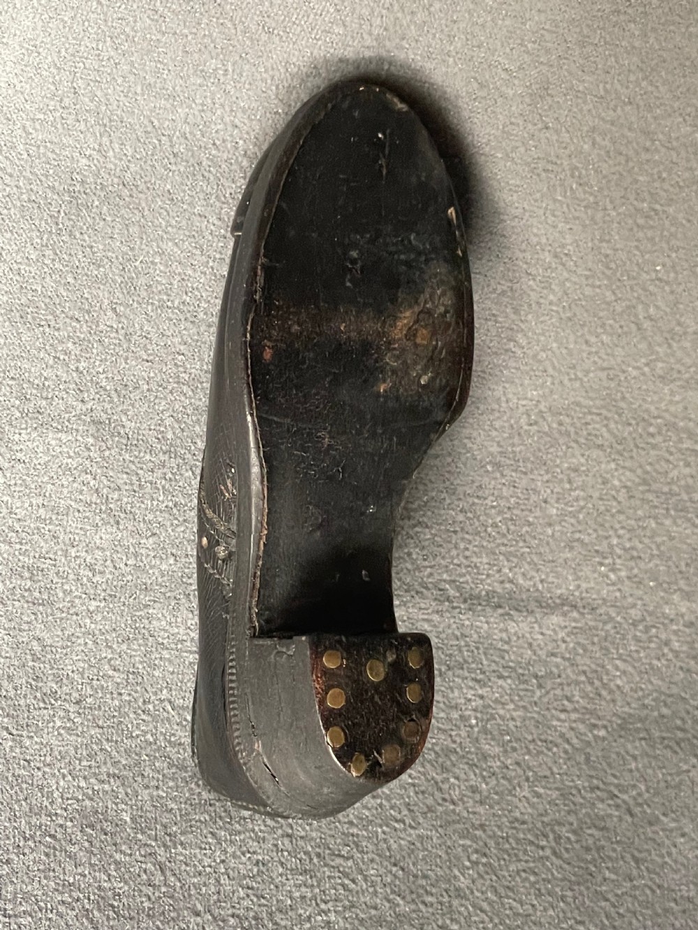 A miniature black leather shoe crafted with brogue stitching and metal eyelets displayed next to a coin for scale. View XIV
