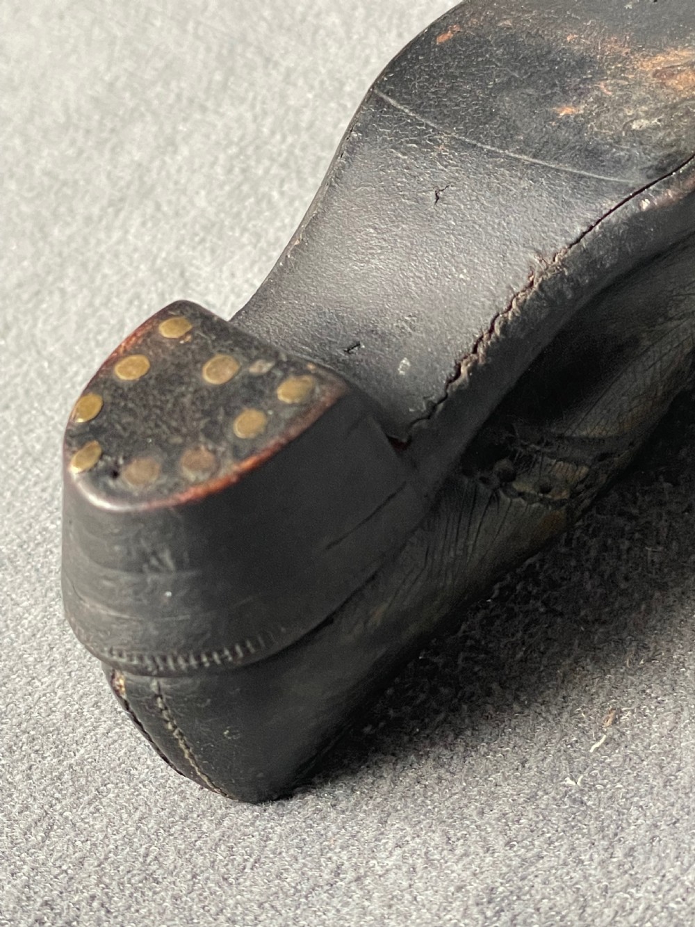 A miniature black leather shoe crafted with brogue stitching and metal eyelets displayed next to a coin for scale. View XV