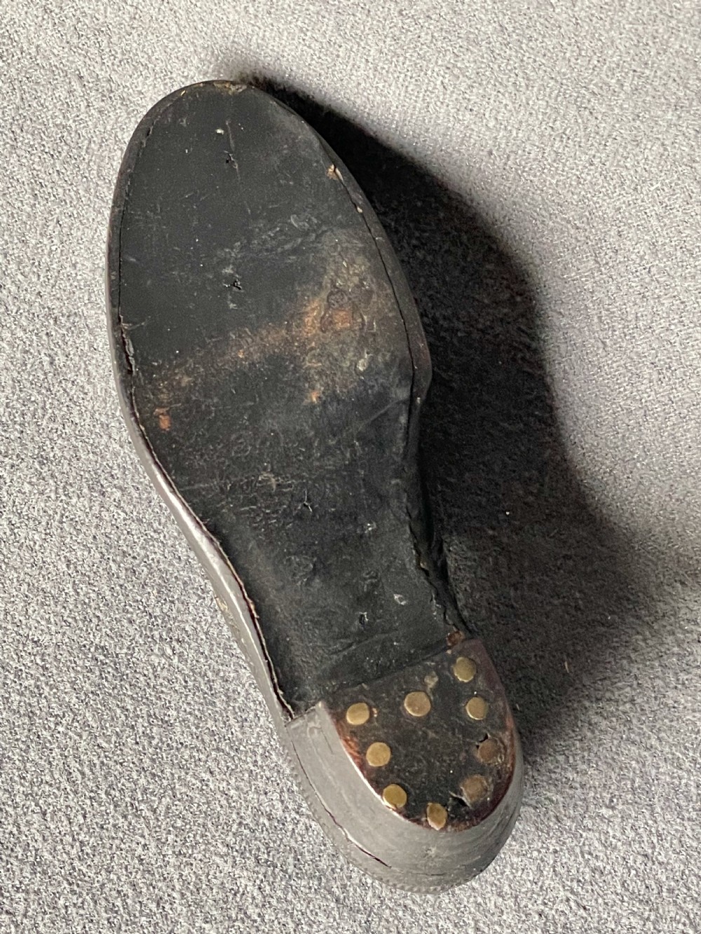 A miniature black leather shoe crafted with brogue stitching and metal eyelets displayed next to a coin for scale. View XVI