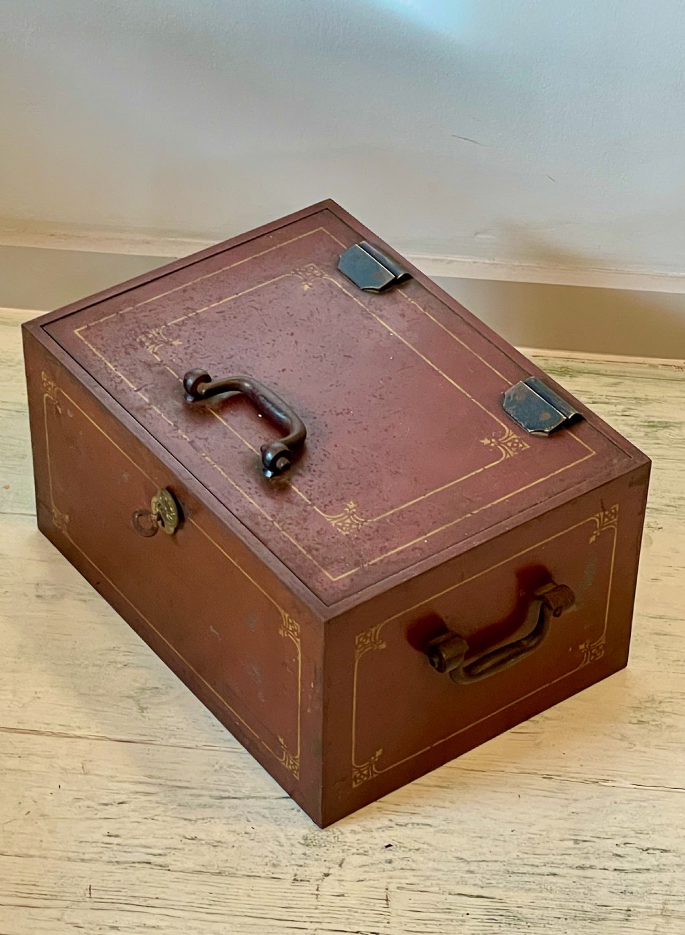 A rectangular terracotta red painted iron strongbox with gilt corner borders, top handle, side carrying handles, and a central brass keyhole escutcheon. View VIII