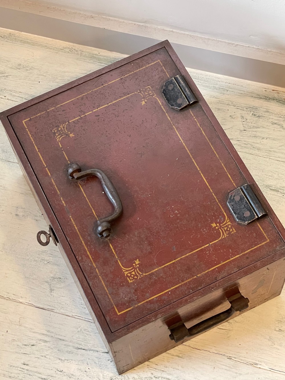 A rectangular terracotta red painted iron strongbox with gilt corner borders, top handle, side carrying handles, and a central brass keyhole escutcheon. View IX