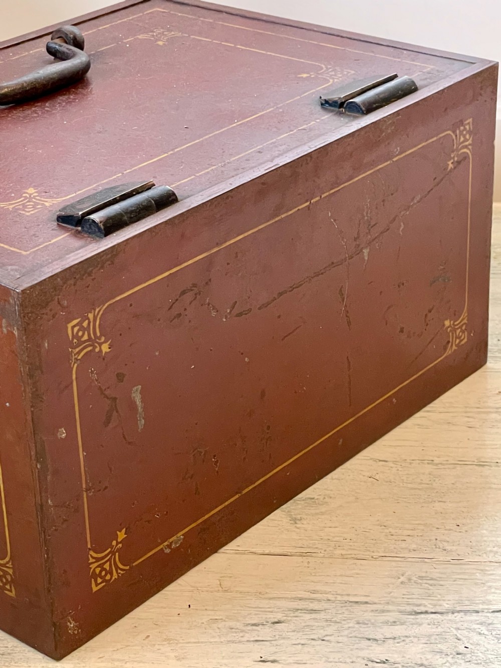 A rectangular terracotta red painted iron strongbox with gilt corner borders, top handle, side carrying handles, and a central brass keyhole escutcheon. View XI