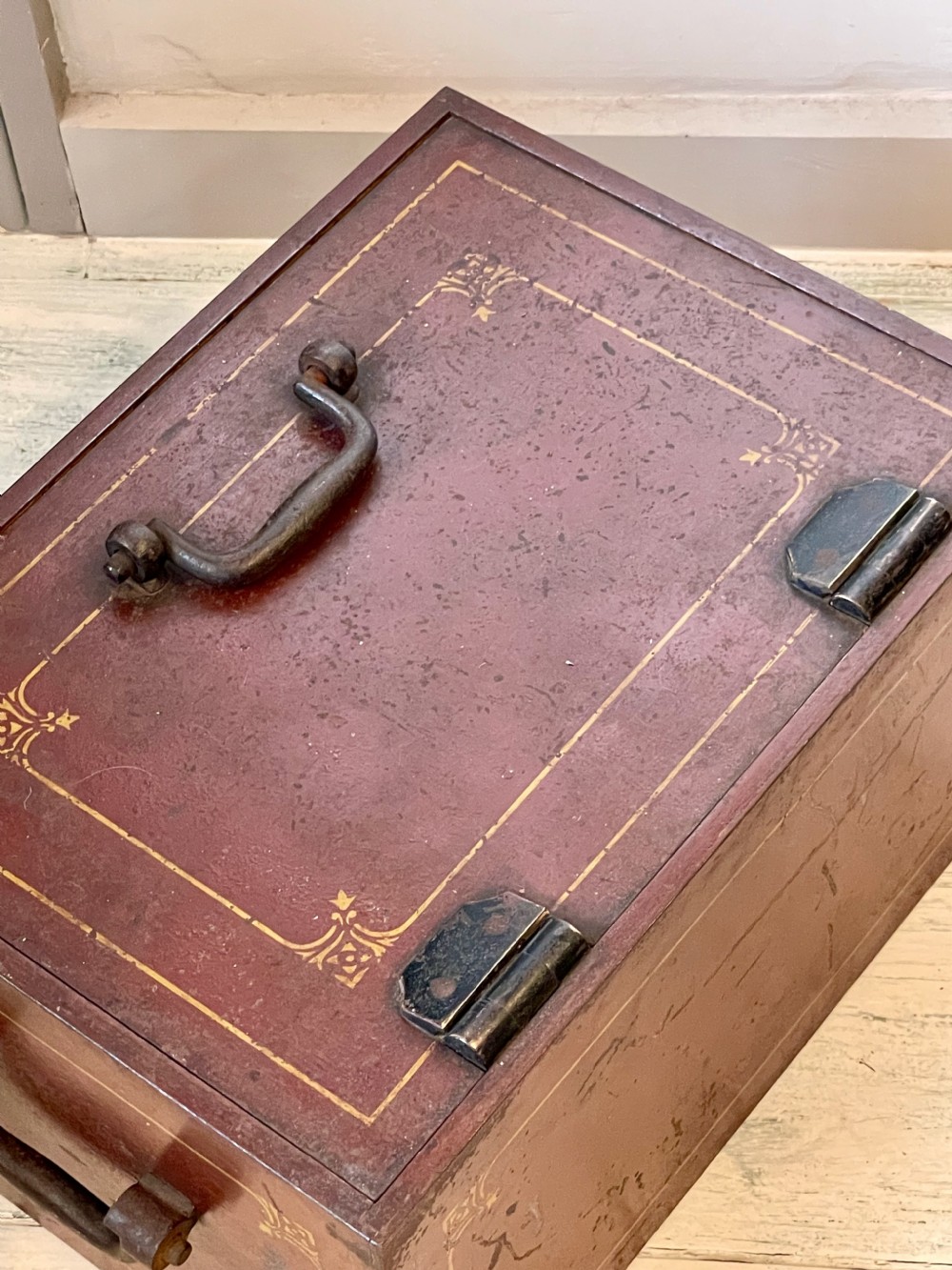 A rectangular terracotta red painted iron strongbox with gilt corner borders, top handle, side carrying handles, and a central brass keyhole escutcheon. View XII