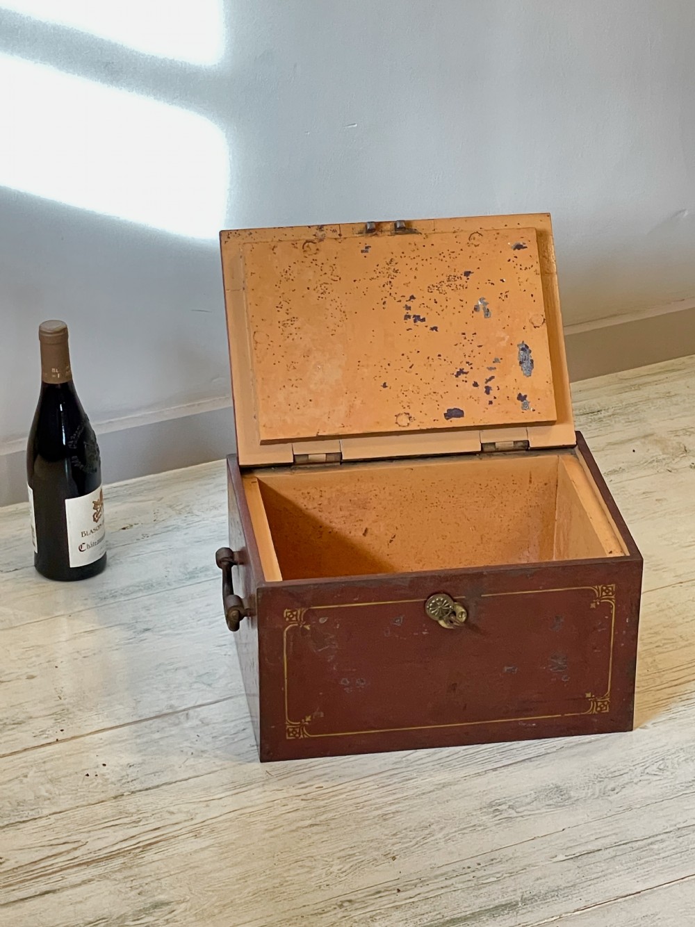 A rectangular terracotta red painted iron strongbox with gilt corner borders, top handle, side carrying handles, and a central brass keyhole escutcheon. View XIV