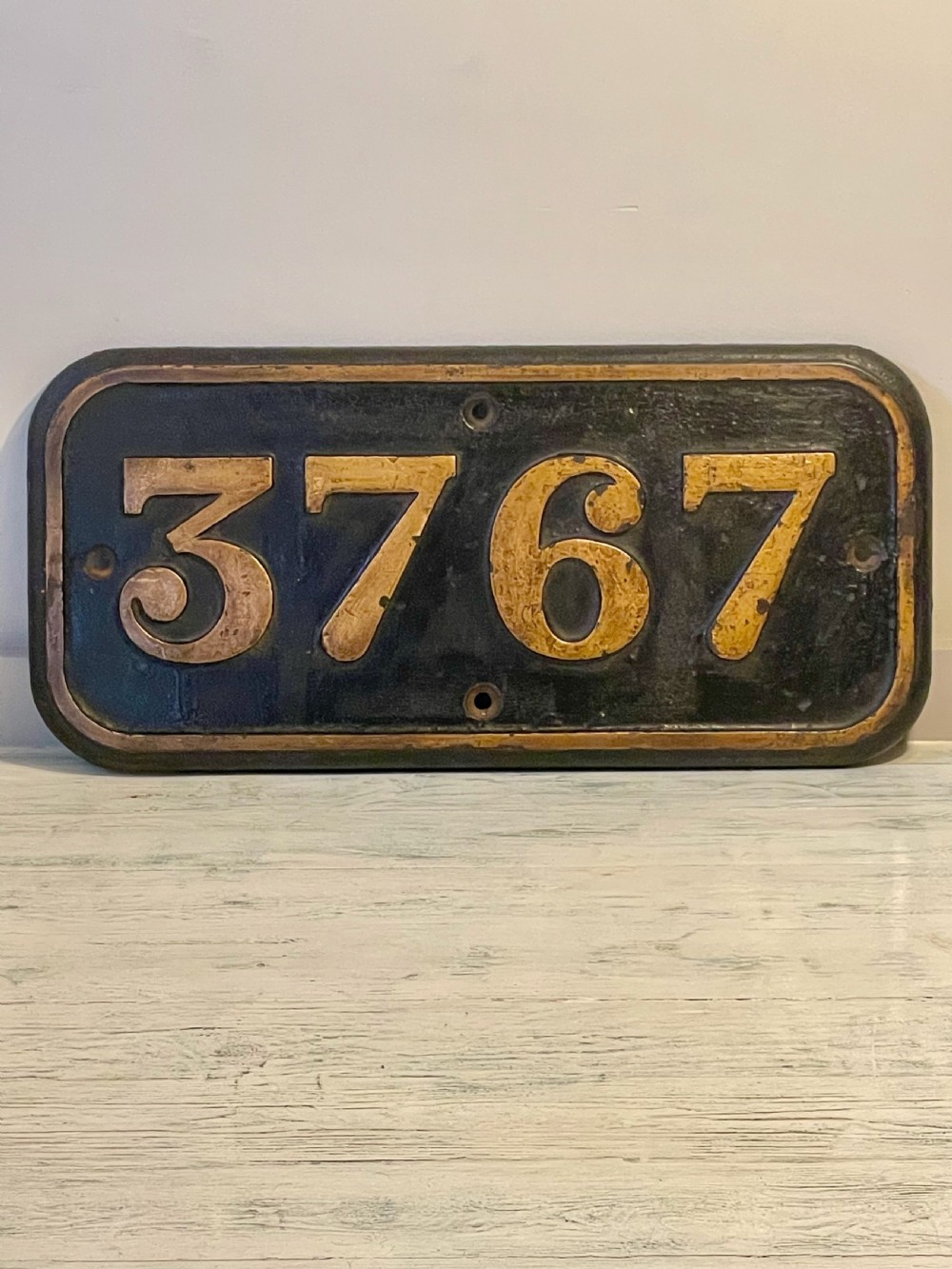 A rectangular cast metal locomotive number plate featuring raised digits 3767 in gold tone against a black background.
