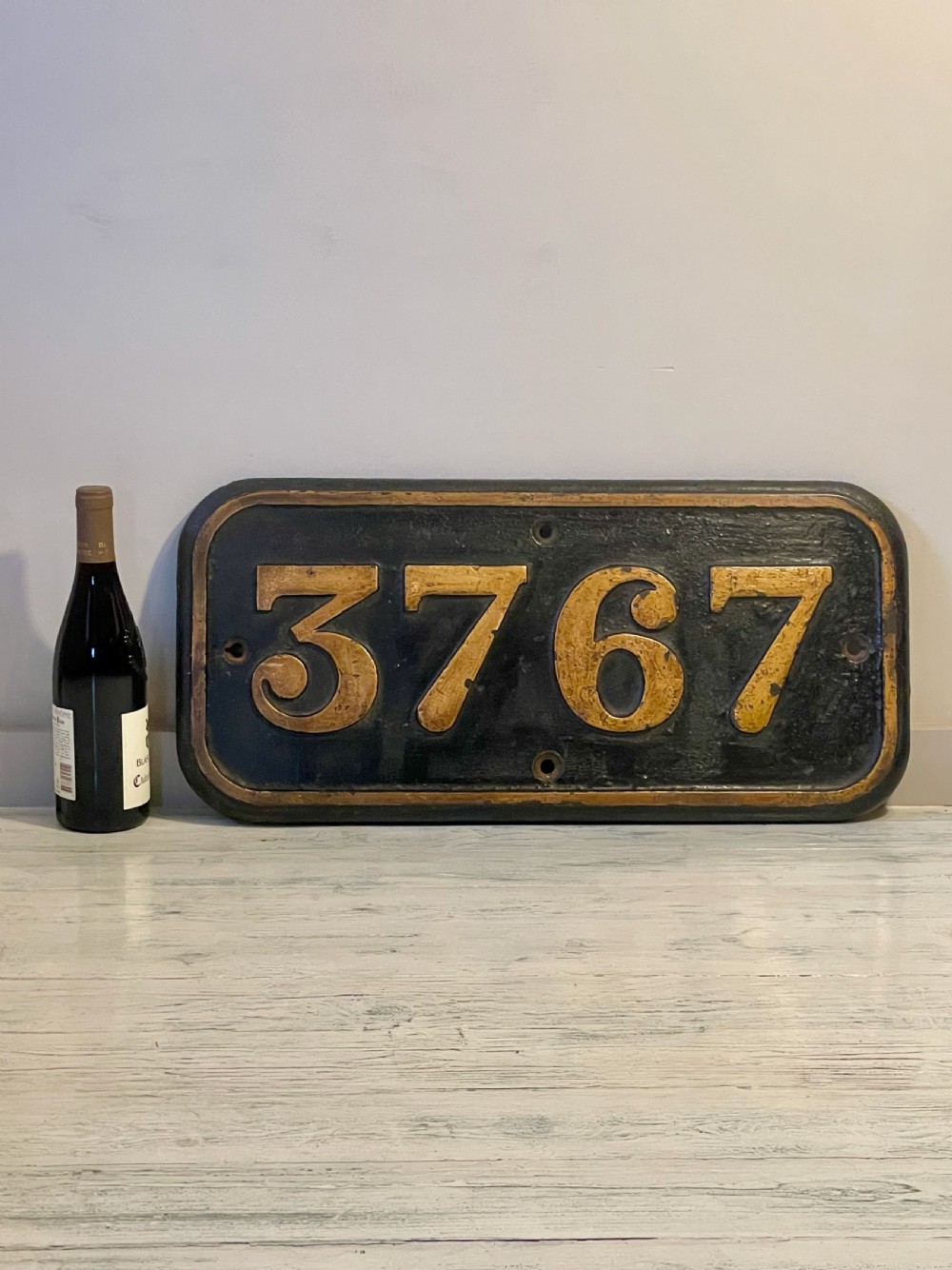 A rectangular cast metal locomotive number plate featuring raised digits 3767 in gold tone against a black background. View II
