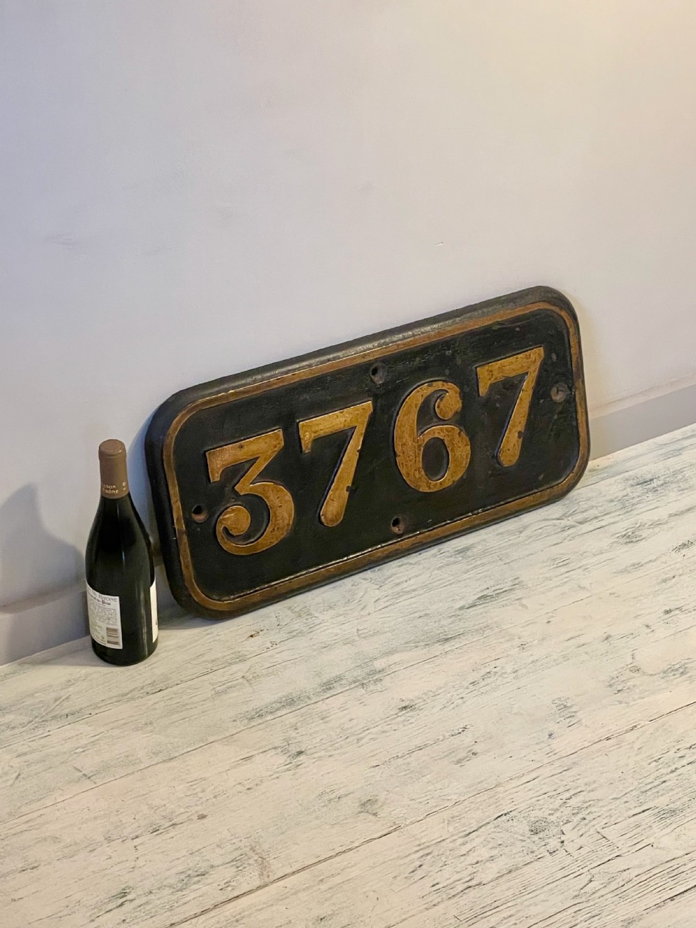 A rectangular cast metal locomotive number plate featuring raised digits 3767 in gold tone against a black background. View IV