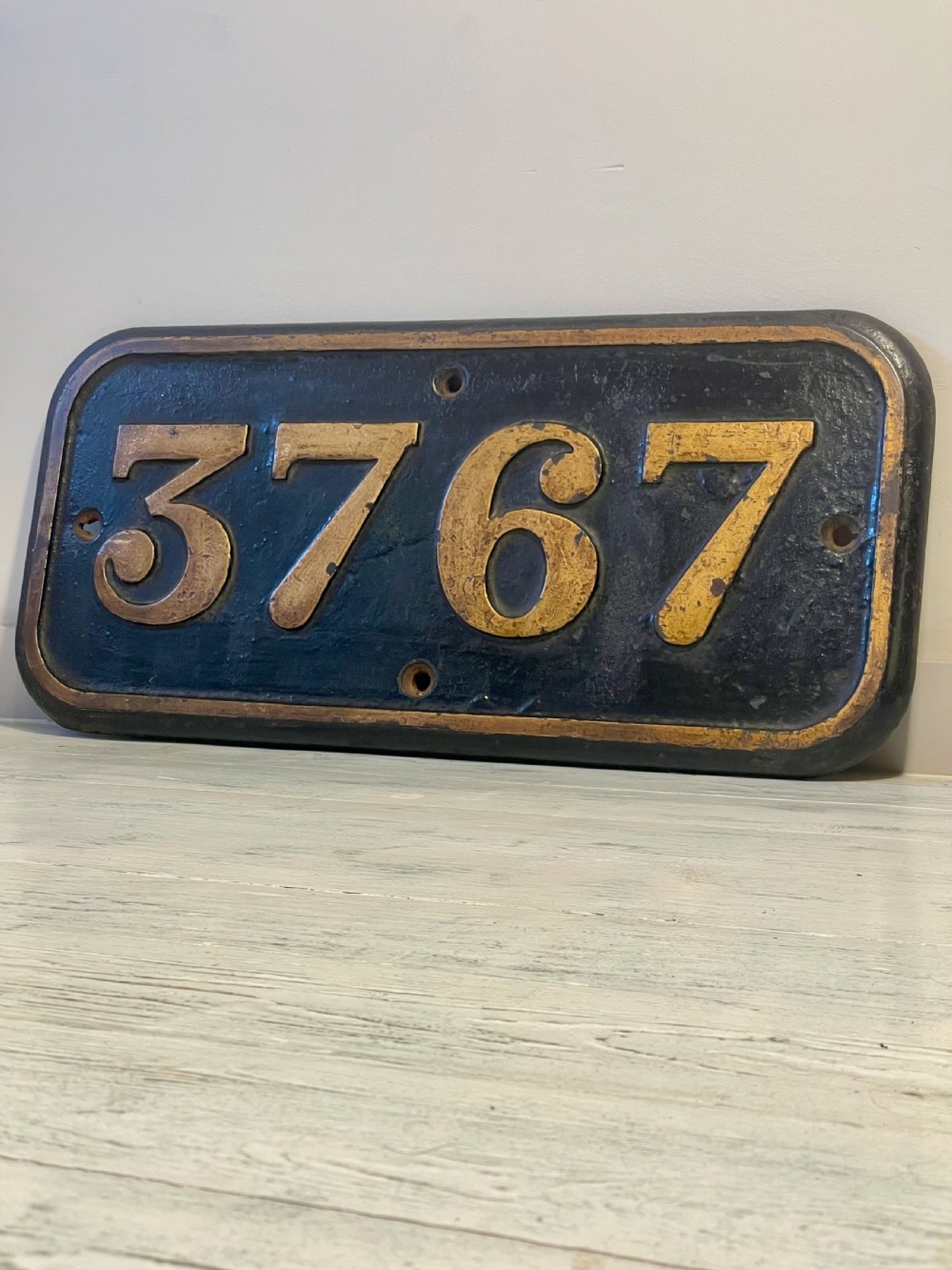 A rectangular cast metal locomotive number plate featuring raised digits 3767 in gold tone against a black background. View VII