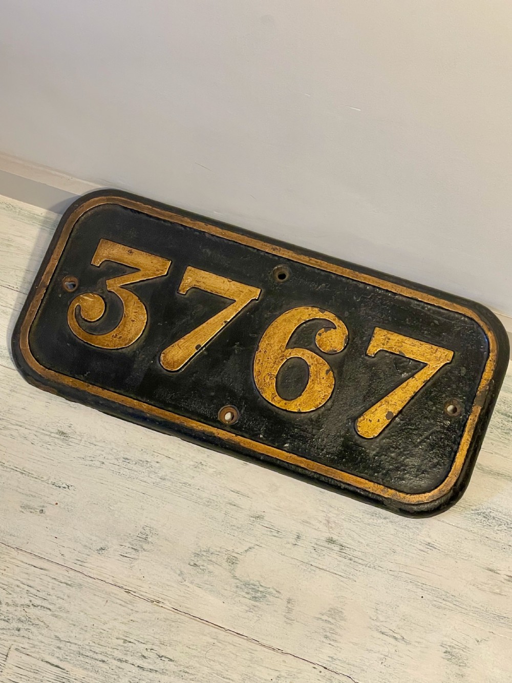 A rectangular cast metal locomotive number plate featuring raised digits 3767 in gold tone against a black background. View XII