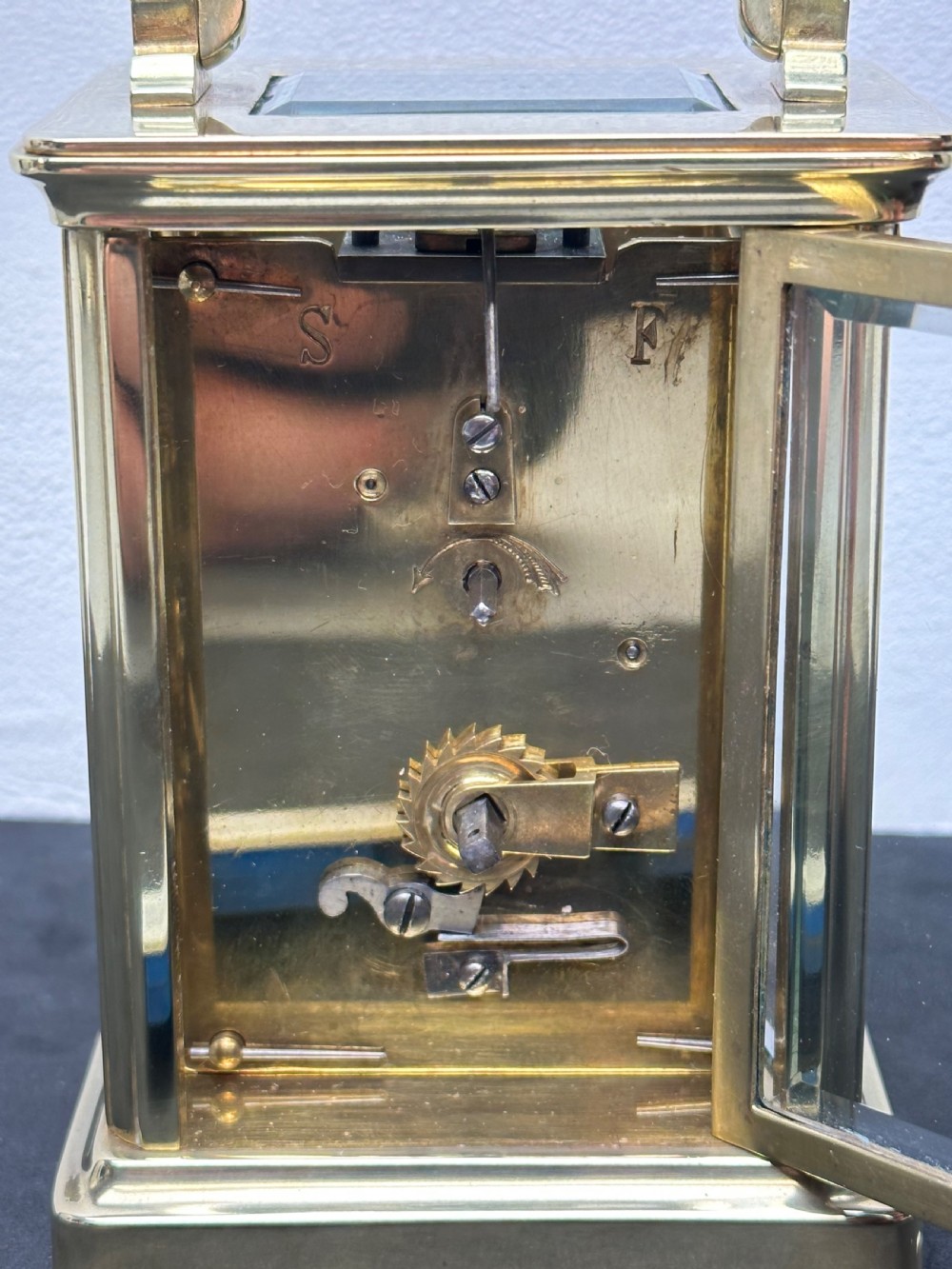 A rectangular brass French carriage clock with clear glass panels, a top carrying handle, and a white enamel dial with black Roman numerals. View III
