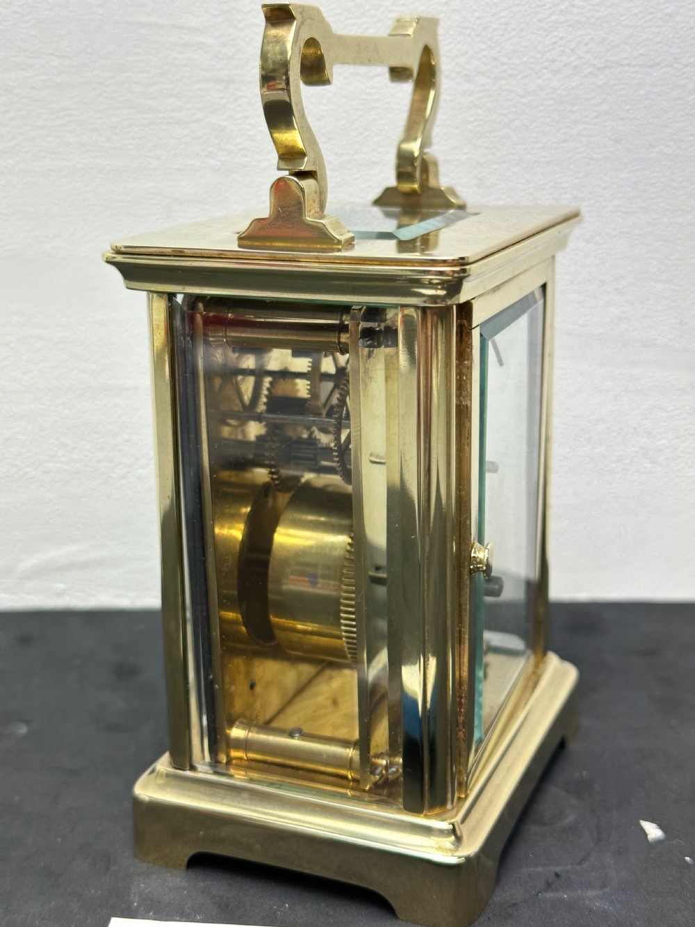 A rectangular brass French carriage clock with clear glass panels, a top carrying handle, and a white enamel dial with black Roman numerals. View V