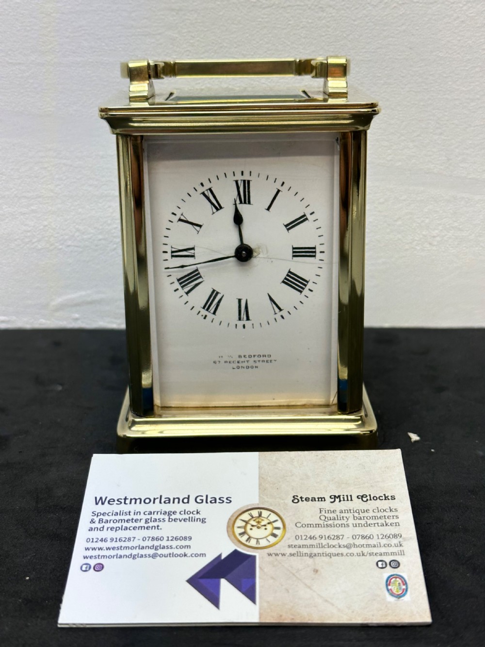 A rectangular brass French carriage clock with clear glass panels, a top carrying handle, and a white enamel dial with black Roman numerals. View VII