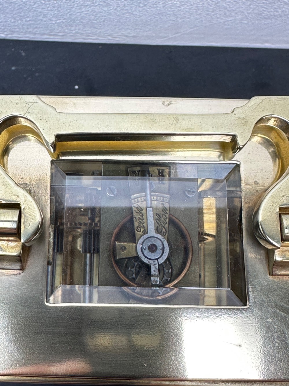 A rectangular brass French carriage clock with clear glass panels, a top carrying handle, and a white enamel dial with black Roman numerals. View VIII