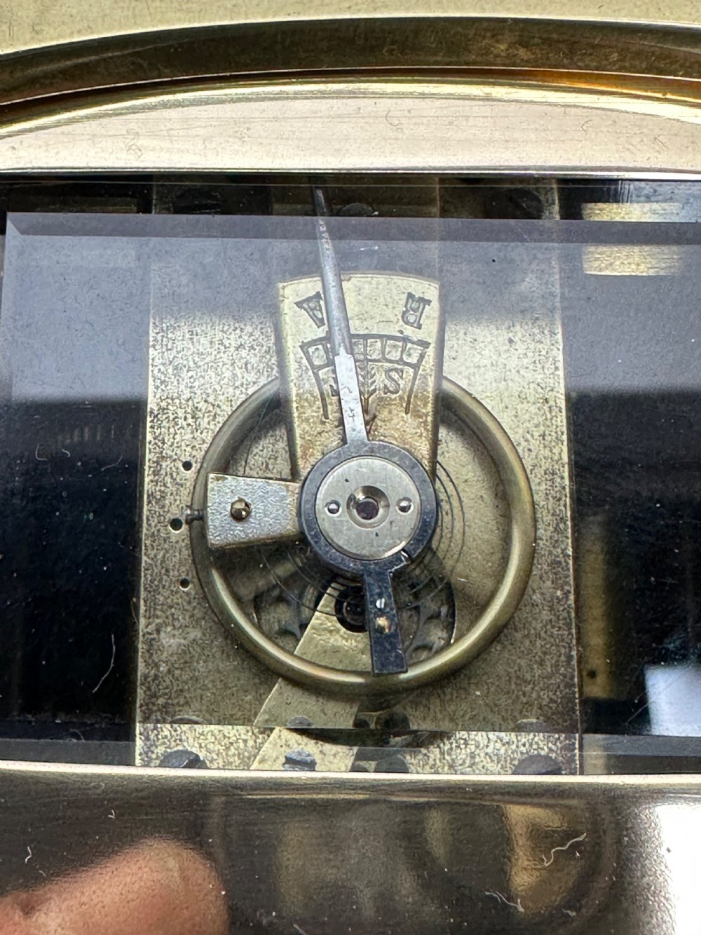 A small rectangular brass carriage clock featuring a top handle, decorative finials, and a white dial with black Arabic numerals. View VIII