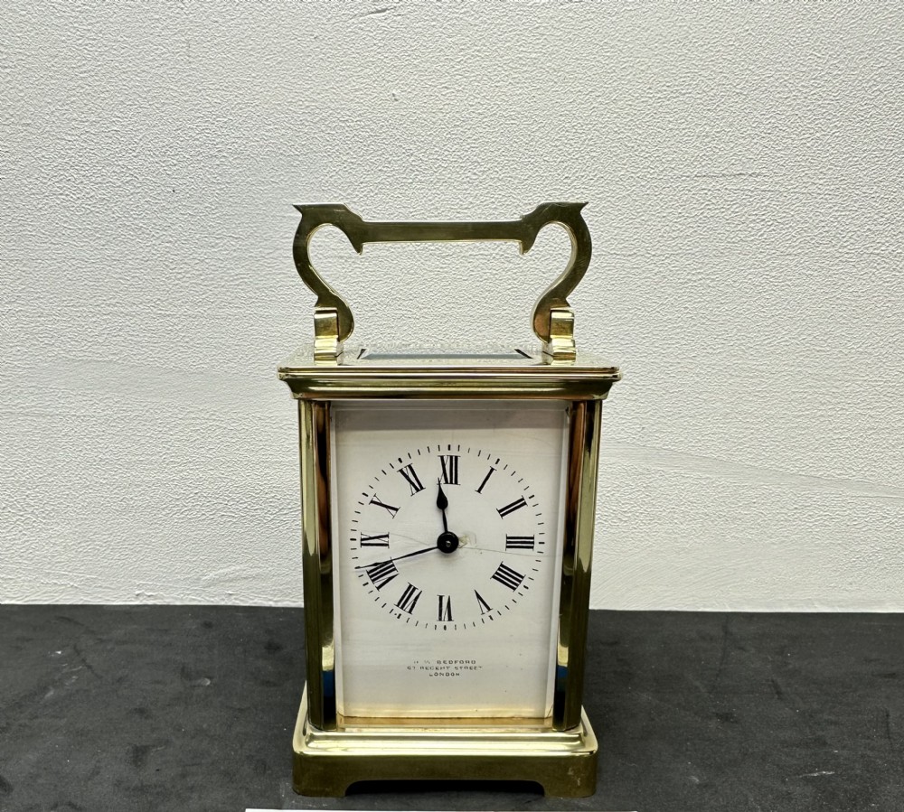 A rectangular brass French carriage clock with clear glass panels, a top carrying handle, and a white enamel dial with black Roman numerals.