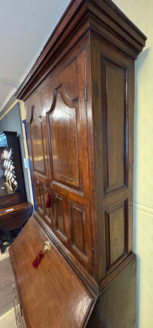 An 18th-century dark oak bureau bookcase featuring an upper cabinet with double panelled doors above a slant-front writing desk and lower drawers with brass handles. View X