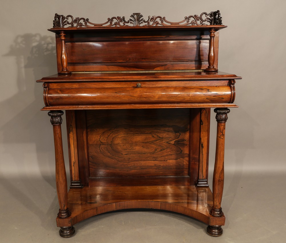 An antique William IV rosewood chiffonier featuring a carved scroll gallery back shelf, turned columns with carved capitals, a cushion frieze drawer, and a concave base.