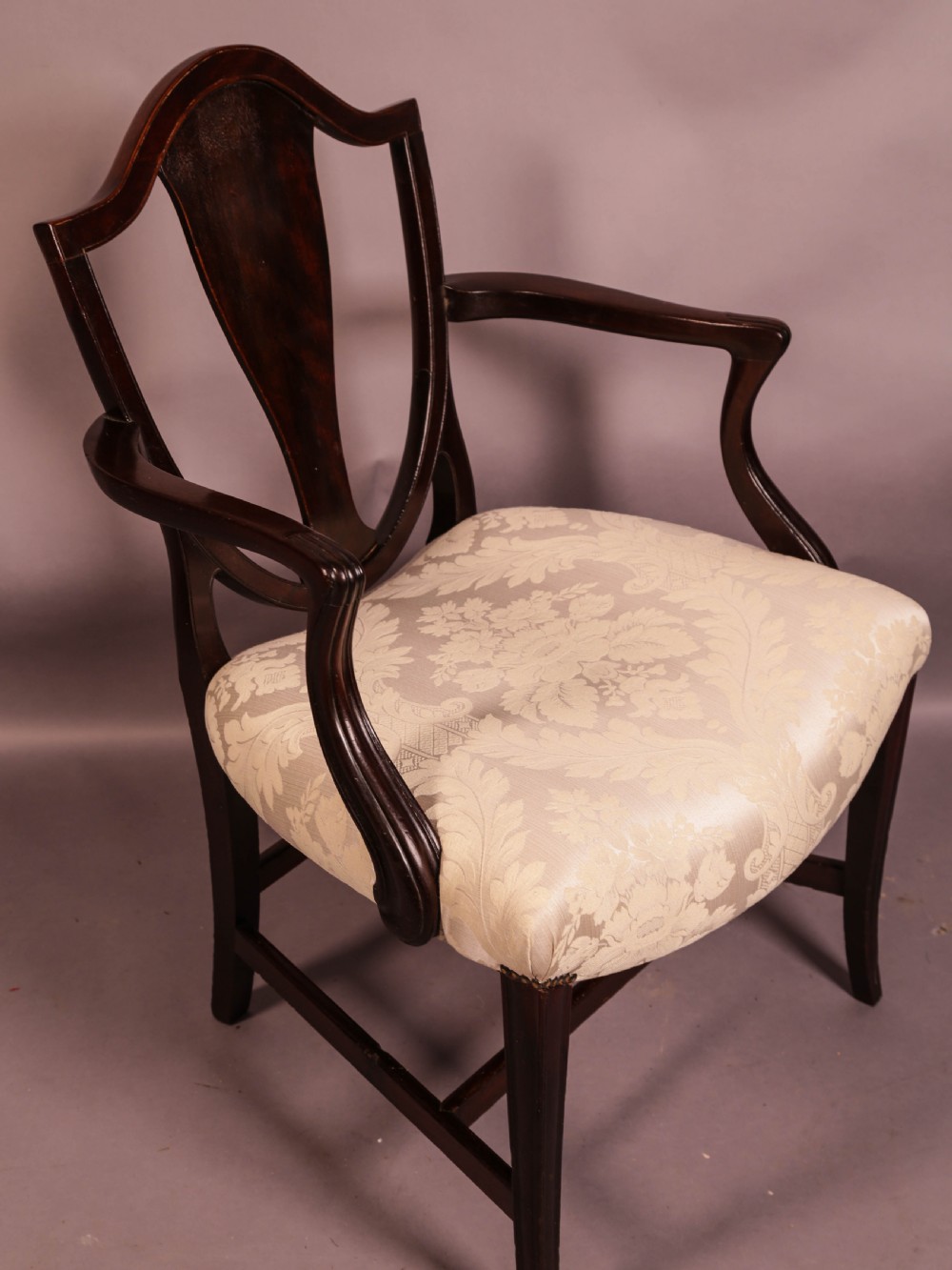 A dark mahogany Hepplewhite period carver armchair featuring a carved open backrest, curved arms, and a cream patterned damask seat. View II