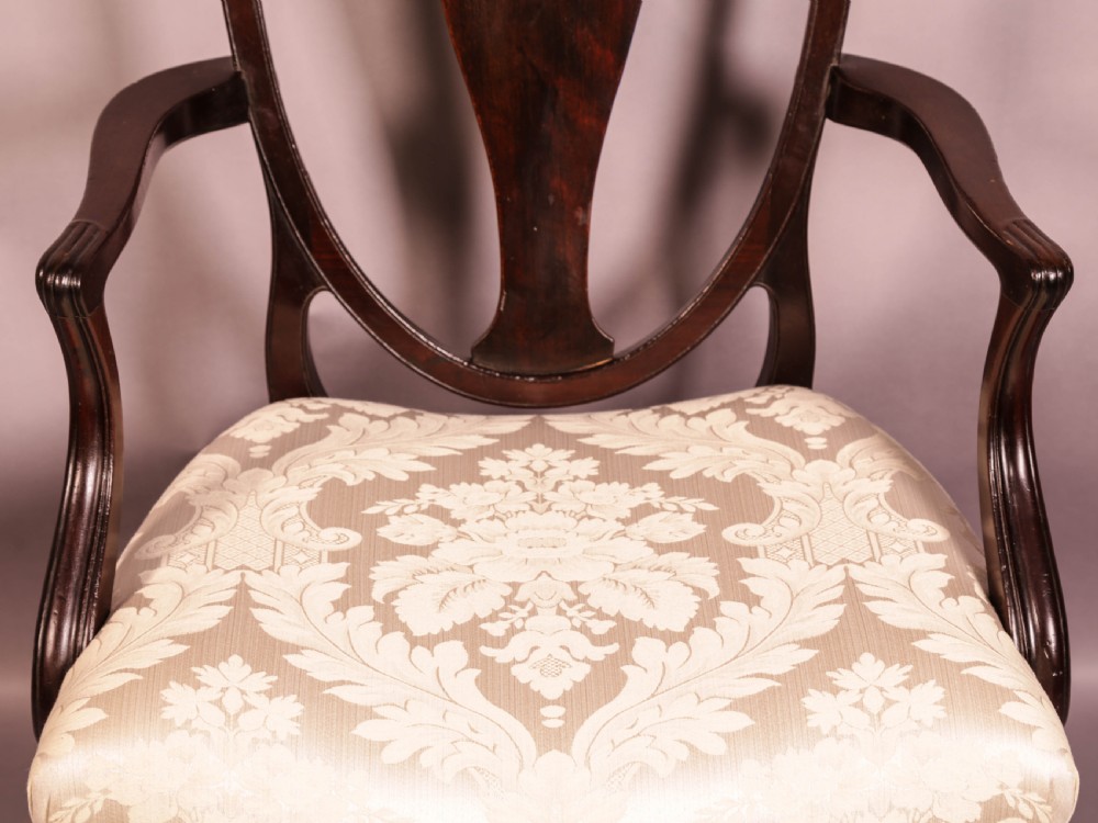 A dark mahogany Hepplewhite period carver armchair featuring a carved open backrest, curved arms, and a cream patterned damask seat. View IV
