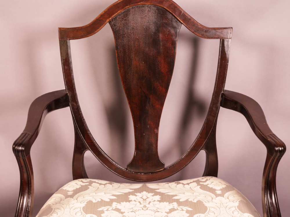 A dark mahogany Hepplewhite period carver armchair featuring a carved open backrest, curved arms, and a cream patterned damask seat. View V