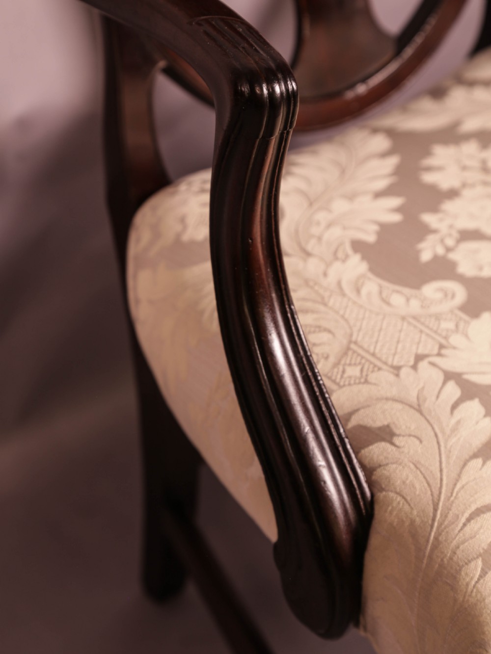 A dark mahogany Hepplewhite period carver armchair featuring a carved open backrest, curved arms, and a cream patterned damask seat. View VII
