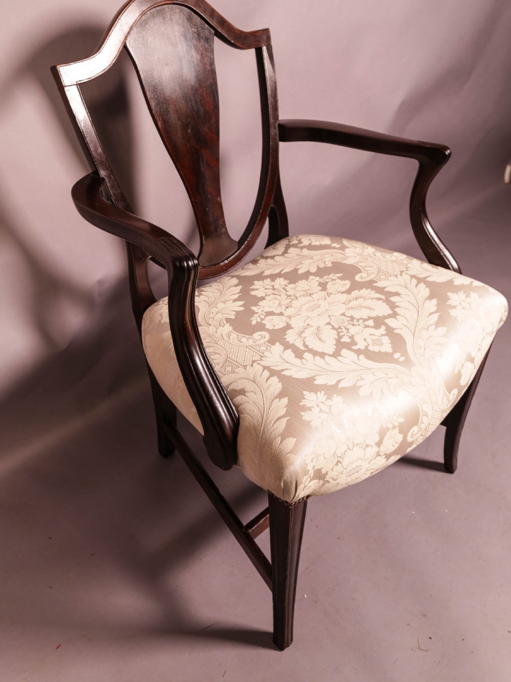 A dark mahogany Hepplewhite period carver armchair featuring a carved open backrest, curved arms, and a cream patterned damask seat. View VIII