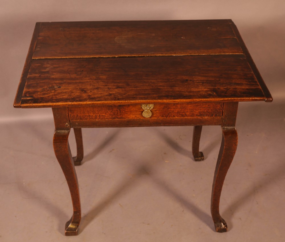 An early 18th-century dark oak side table featuring cabriole legs, a single frieze drawer, and a brass drop handle.