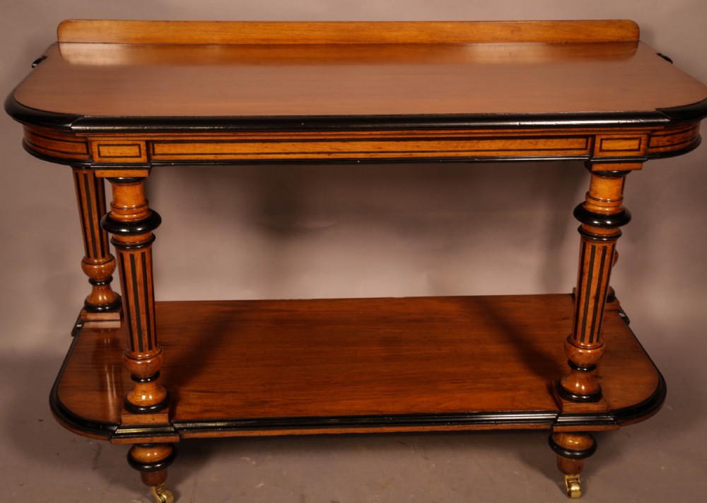 An Aesthetic Movement walnut serving table featuring a rectangular top with a low gallery, ebonised trim, a full lower tier, and turned fluted legs on brass castors. View III
