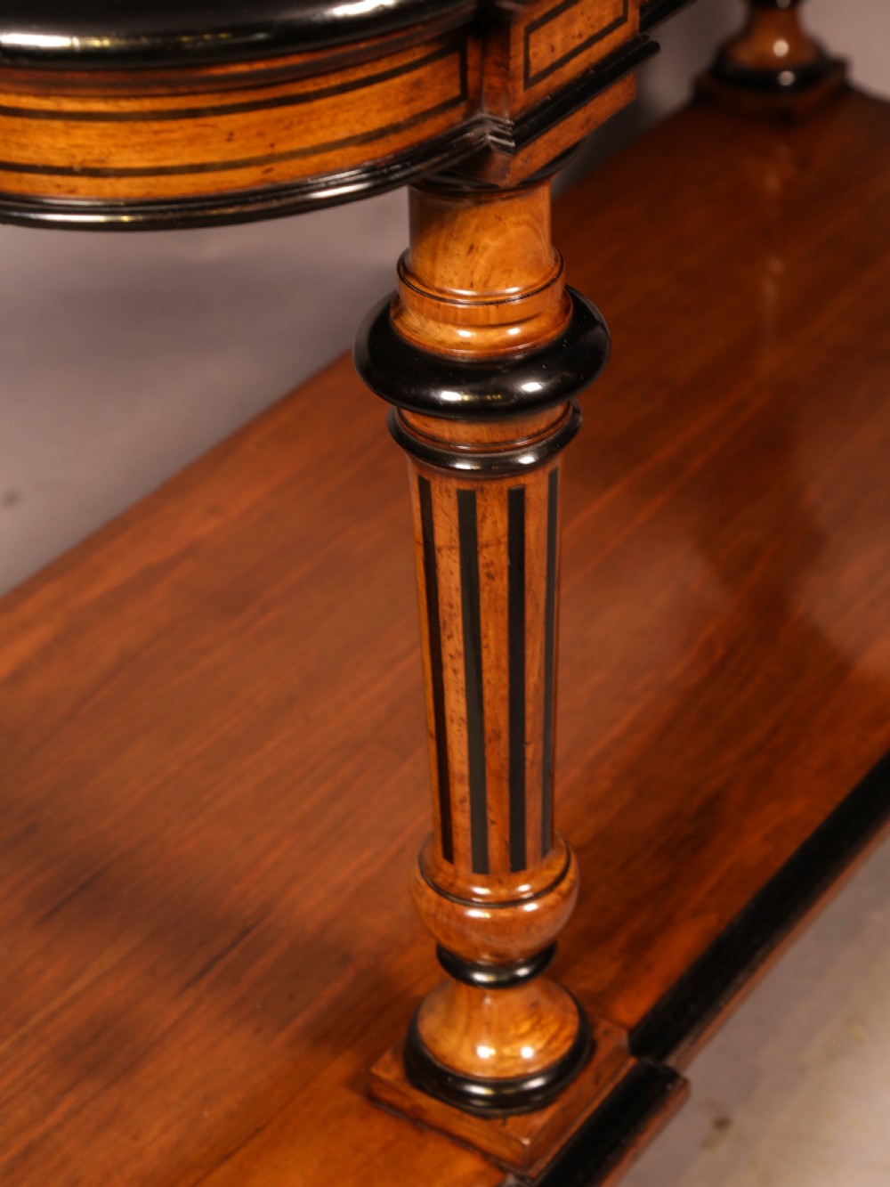 An Aesthetic Movement walnut serving table featuring a rectangular top with a low gallery, ebonised trim, a full lower tier, and turned fluted legs on brass castors. View VIII