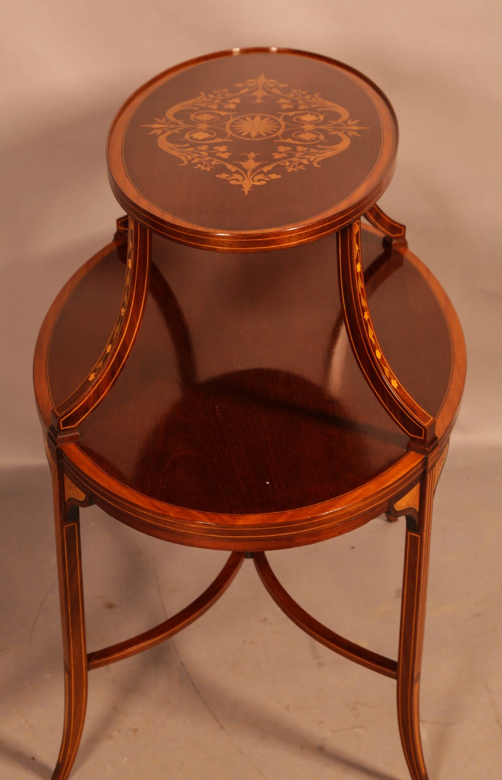 An Edwardian two-tier oval mahogany etagere featuring detailed central floral marquetry inlay, slender curved supports, and swept legs with crossbanding. View III