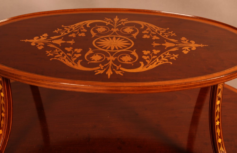 An Edwardian two-tier oval mahogany etagere featuring detailed central floral marquetry inlay, slender curved supports, and swept legs with crossbanding. View IV