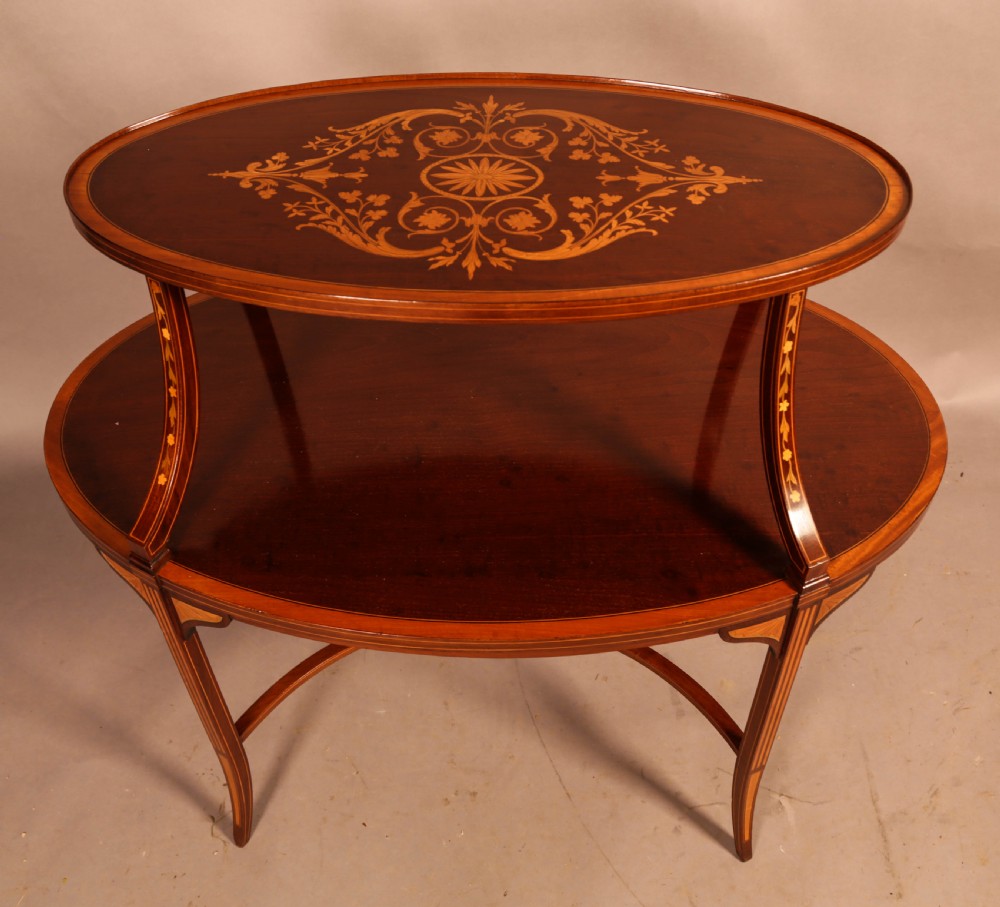 An Edwardian two-tier oval mahogany etagere featuring detailed central floral marquetry inlay, slender curved supports, and swept legs with crossbanding. View V