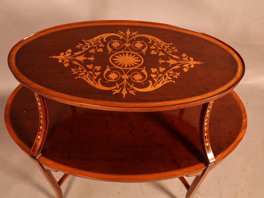 An Edwardian two-tier oval mahogany etagere featuring detailed central floral marquetry inlay, slender curved supports, and swept legs with crossbanding. View VI