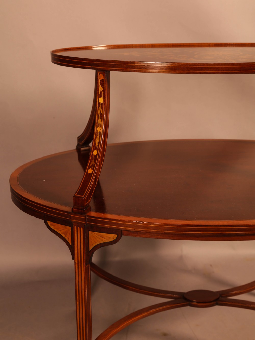 An Edwardian two-tier oval mahogany etagere featuring detailed central floral marquetry inlay, slender curved supports, and swept legs with crossbanding. View XI