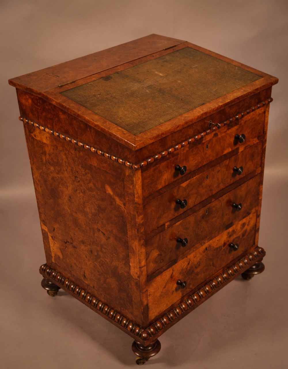 A Victorian burr oak Davenport desk featuring a green leather writing slope, side drawers with wooden knobs, bead moulding, and brass casters. View II