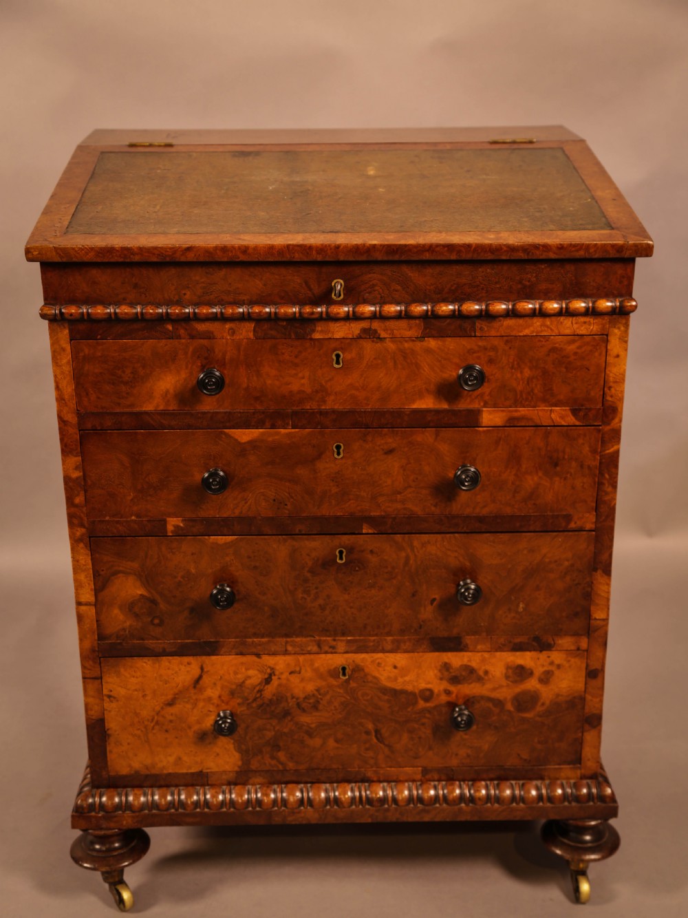 A Victorian burr oak Davenport desk featuring a green leather writing slope, side drawers with wooden knobs, bead moulding, and brass casters. View III