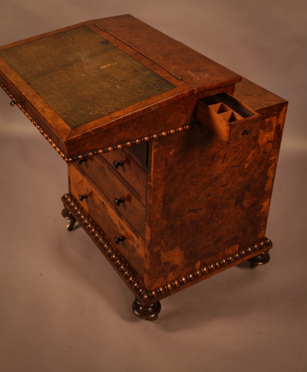 A Victorian burr oak Davenport desk featuring a green leather writing slope, side drawers with wooden knobs, bead moulding, and brass casters. View VIII