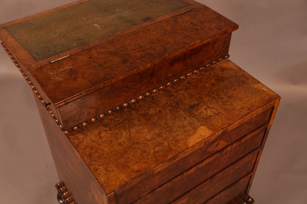 A Victorian burr oak Davenport desk featuring a green leather writing slope, side drawers with wooden knobs, bead moulding, and brass casters. View IX