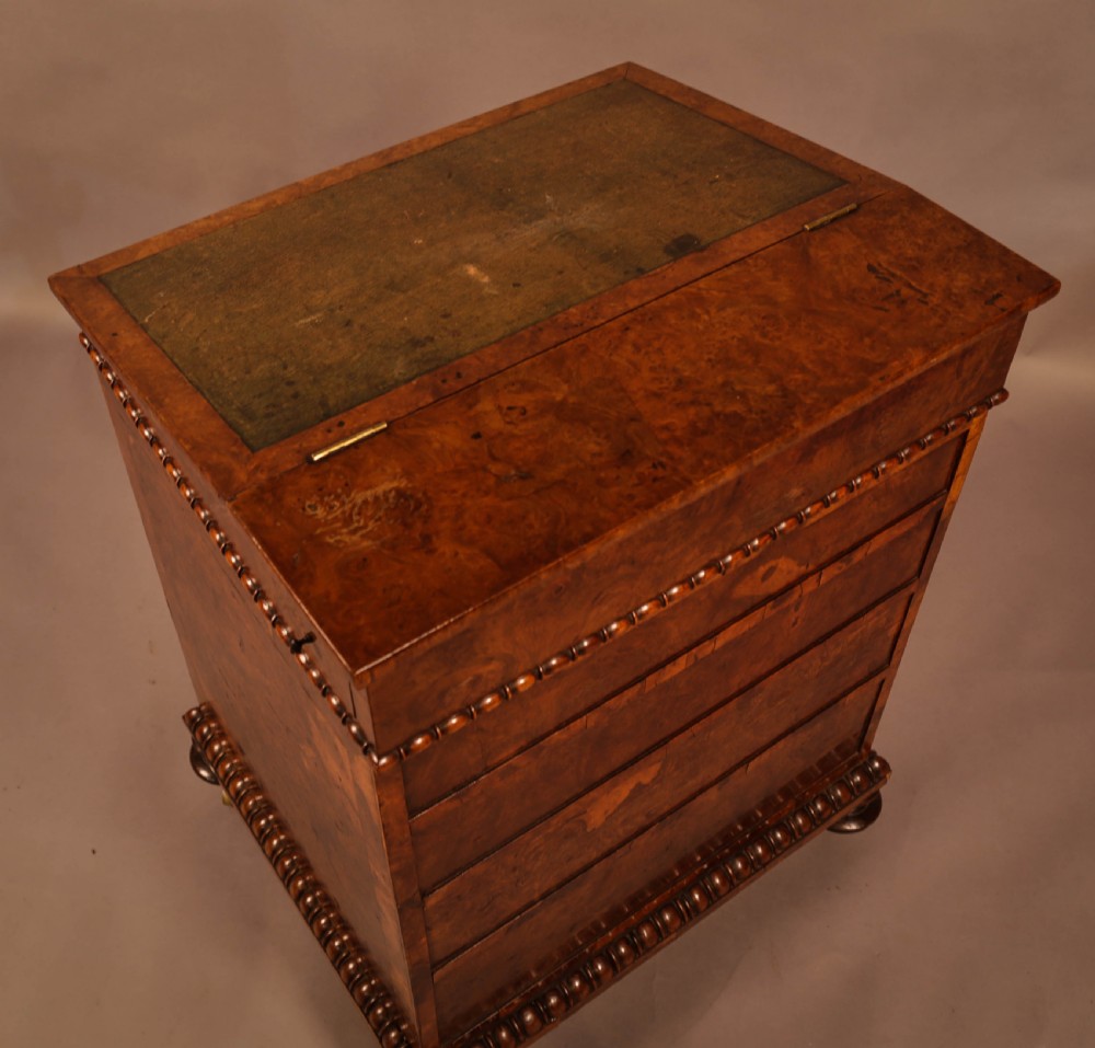 A Victorian burr oak Davenport desk featuring a green leather writing slope, side drawers with wooden knobs, bead moulding, and brass casters. View X