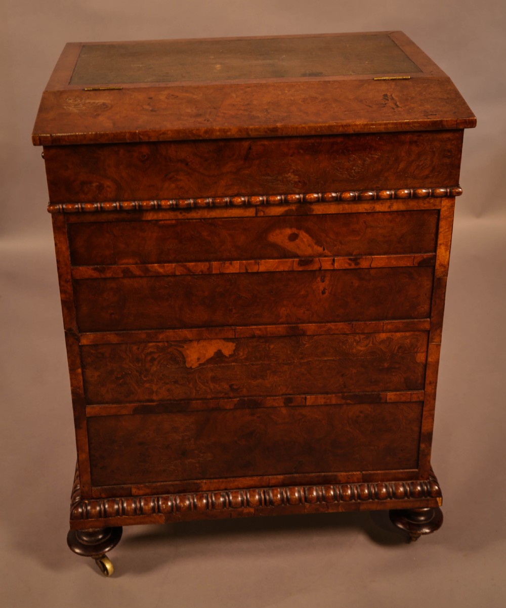 A Victorian burr oak Davenport desk featuring a green leather writing slope, side drawers with wooden knobs, bead moulding, and brass casters. View XI