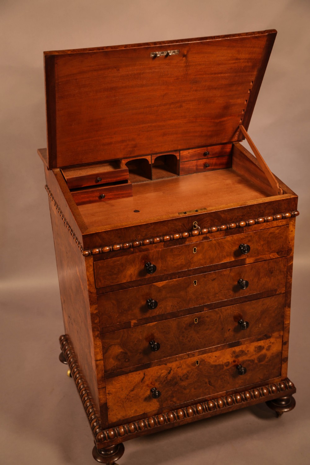A Victorian burr oak Davenport desk featuring a green leather writing slope, side drawers with wooden knobs, bead moulding, and brass casters. View XII