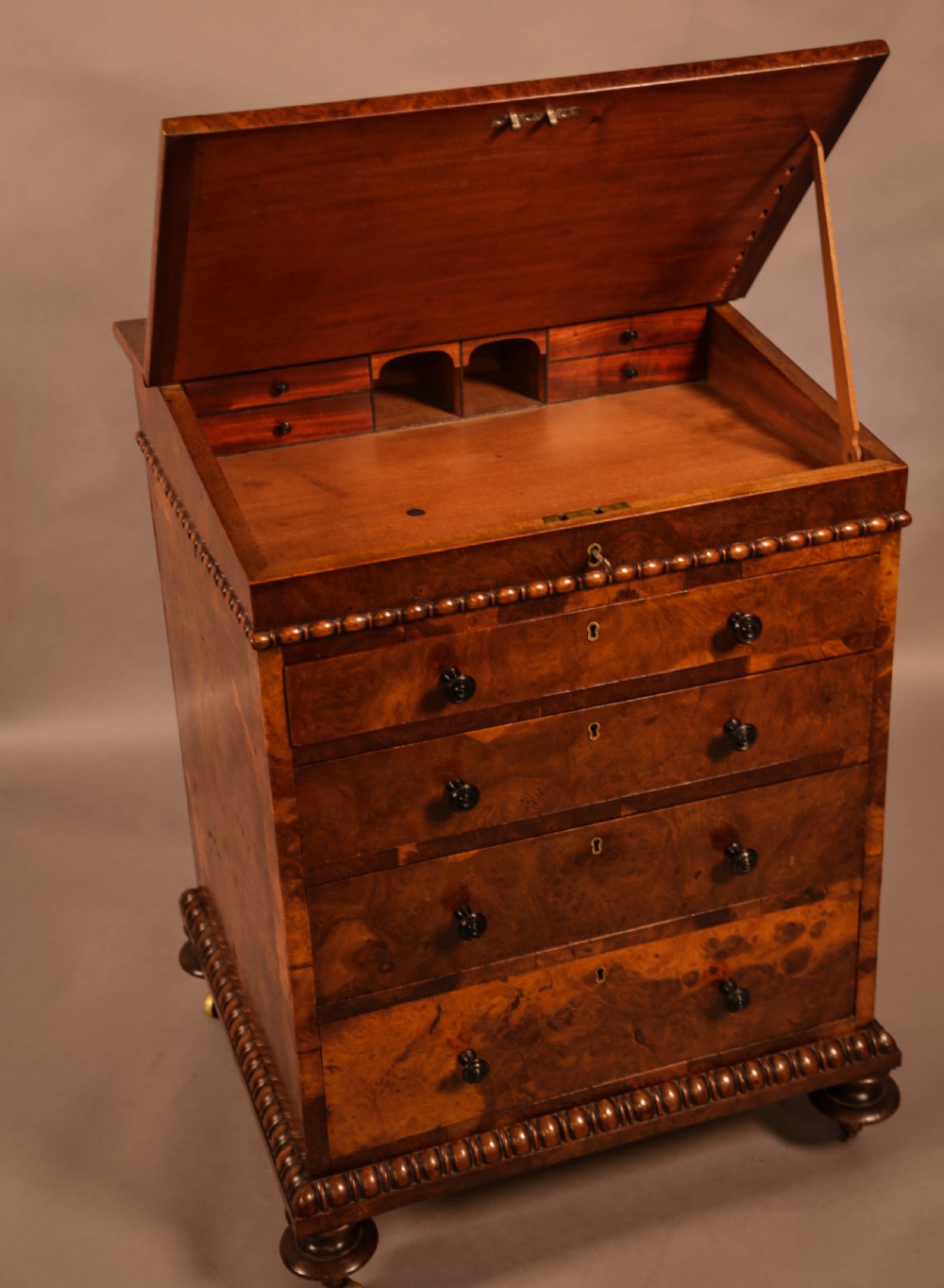 A Victorian burr oak Davenport desk featuring a green leather writing slope, side drawers with wooden knobs, bead moulding, and brass casters. View XIII