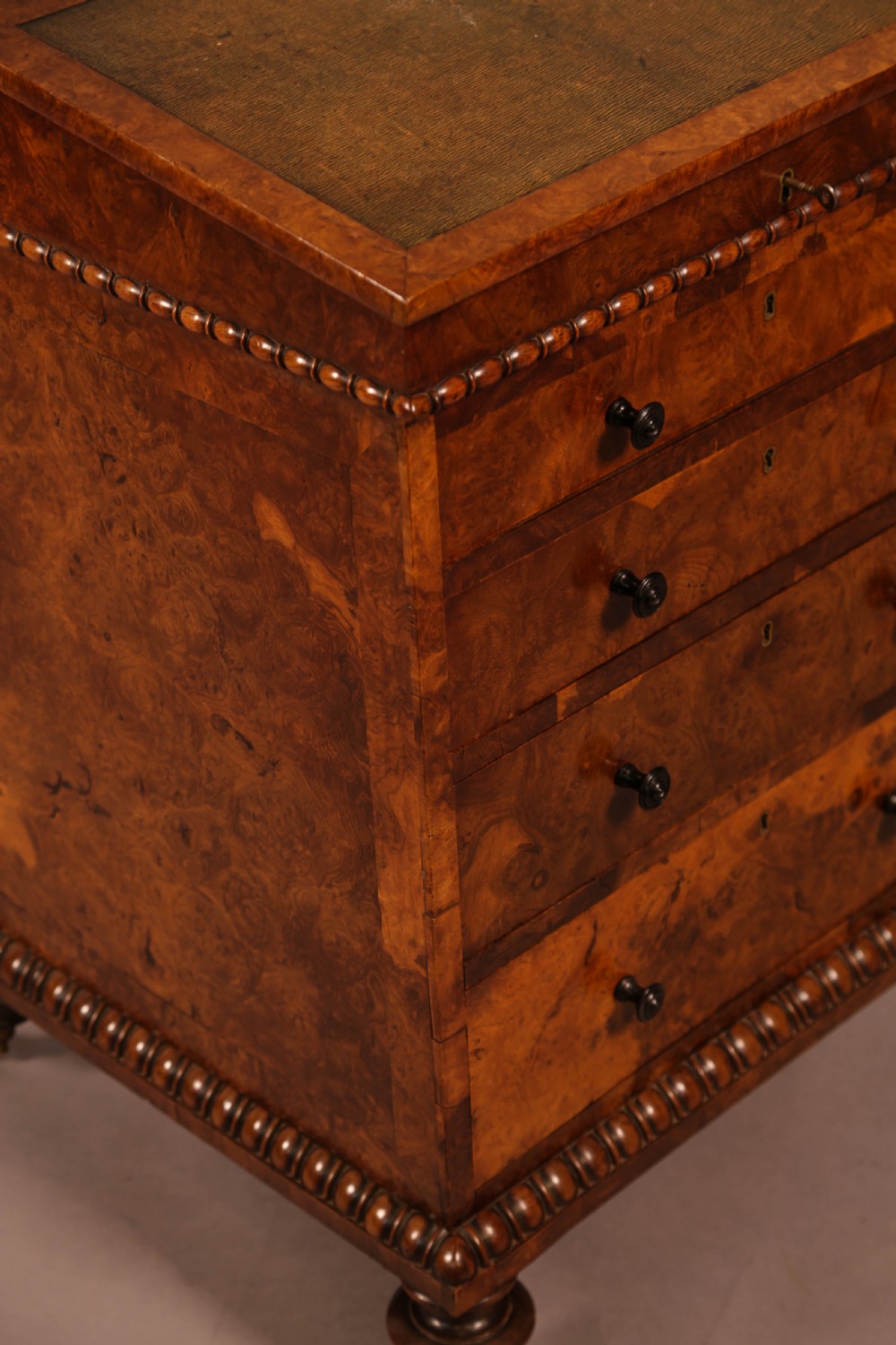 A Victorian burr oak Davenport desk featuring a green leather writing slope, side drawers with wooden knobs, bead moulding, and brass casters. View XIV